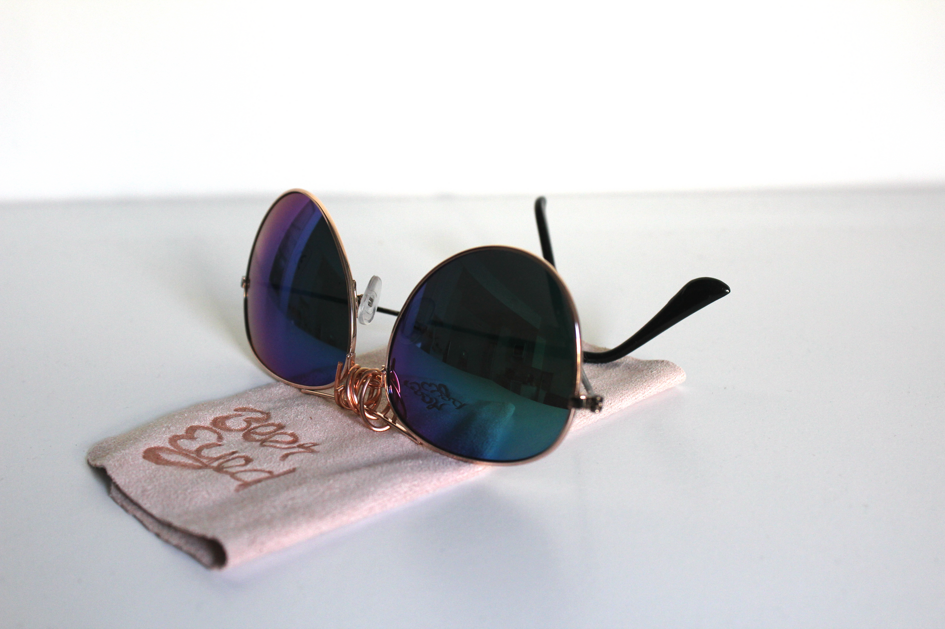 Sunglasses with blue-green lenses and matte-black arms. Beer Eyed sunglasses cloth under sunglasses.