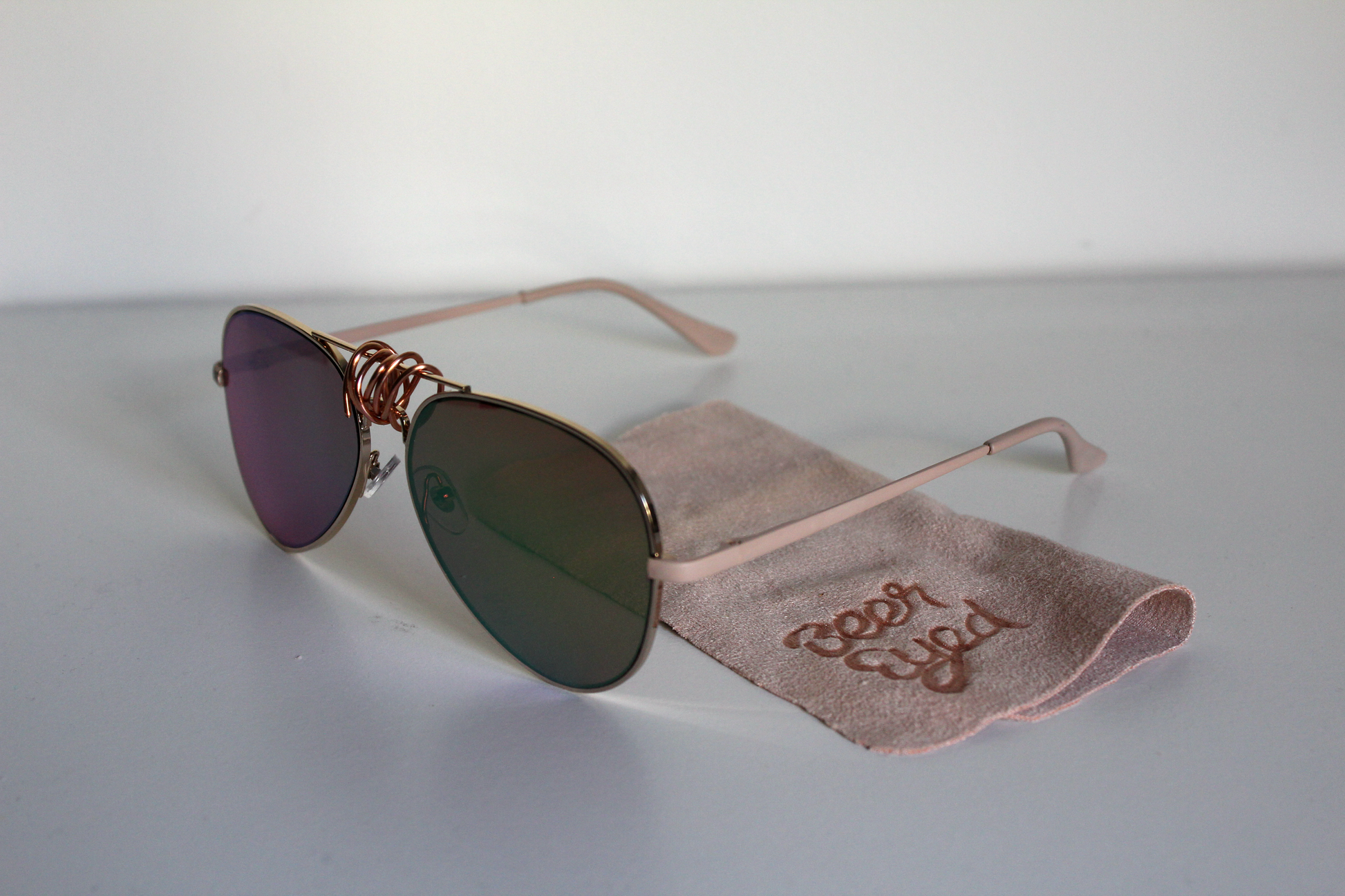 Sunglasses with rose-gold lenses and matte-rose arms.  Beer Eyed sunglasses cloth under sunglasses. Right-view