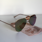 Sunglasses with rose-gold lenses and matte-rose arms.  Beer Eyed sunglasses cloth under sunglasses. Left-view